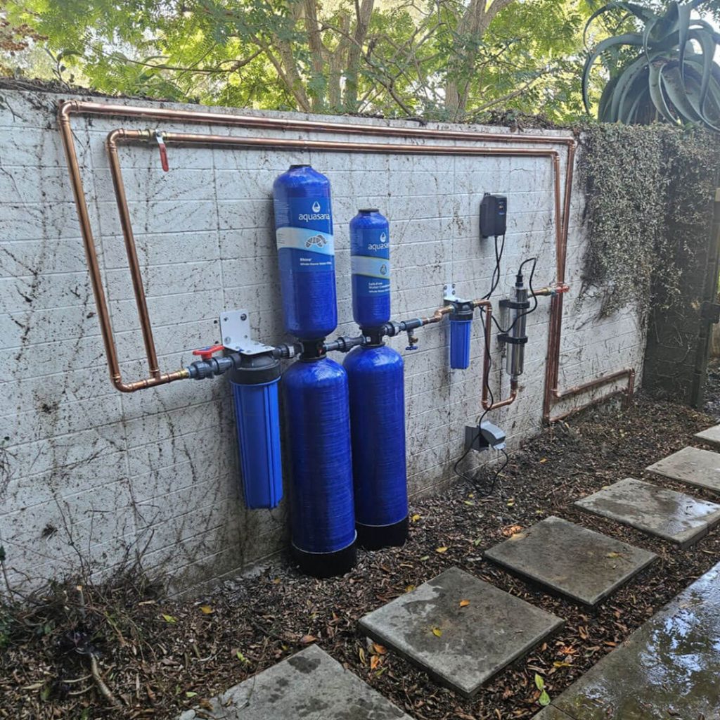 Water filtration system installation featuring blue Aquasana tanks and copper piping, showcasing plumbing expertise and quality service by System Wide Services.